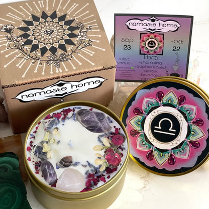 A spiritual candle set by Namaste Home, featuring a gold tin candle with white wax and embedded crystals, its lid shown next with a pink and gold mandala design, a kraft paper box with a black mandala, and a colorful calendar card.