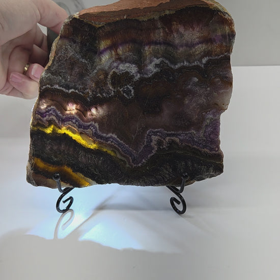 Banded crystal slice with multiple colors and inclusions on a stand against a marble background, being backlit