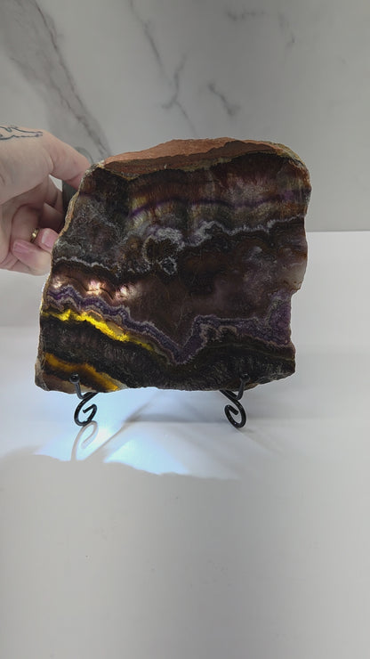Banded crystal slice with multiple colors and inclusions on a stand against a marble background, being backlit