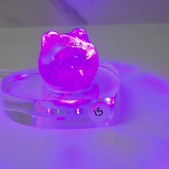 A small purple crystal cluster sculpture displayed on a clear acrylic stand with a white sticker marked '15' on it, set against a plain light gray background.