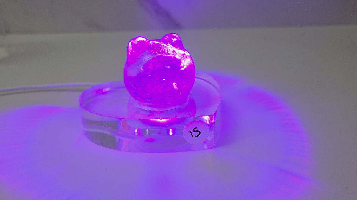 A small purple crystal cluster sculpture displayed on a clear acrylic stand with a white sticker marked '15' on it, set against a plain light gray background.