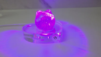 A small purple crystal cluster sculpture displayed on a clear acrylic stand with a white sticker marked '15' on it, set against a plain light gray background.