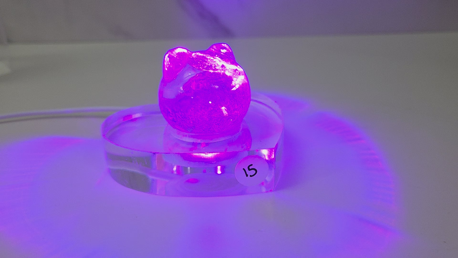 A small purple crystal cluster sculpture displayed on a clear acrylic stand with a white sticker marked '15' on it, set against a plain light gray background.
