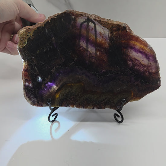 Banded crystal slice with multiple colors and inclusions on a stand against a marble background, being backlit